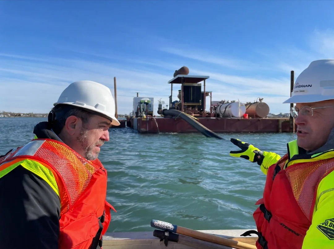 Engineers in hard hats beside a J.F. Brennan dredging vessel on the water