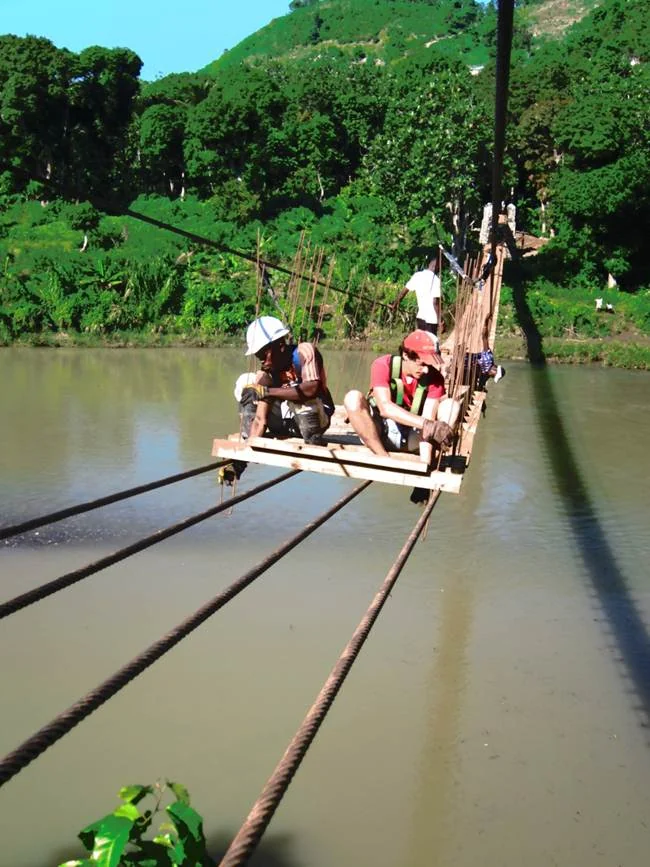 Workers building a pedestrian bridge over a river in Haiti